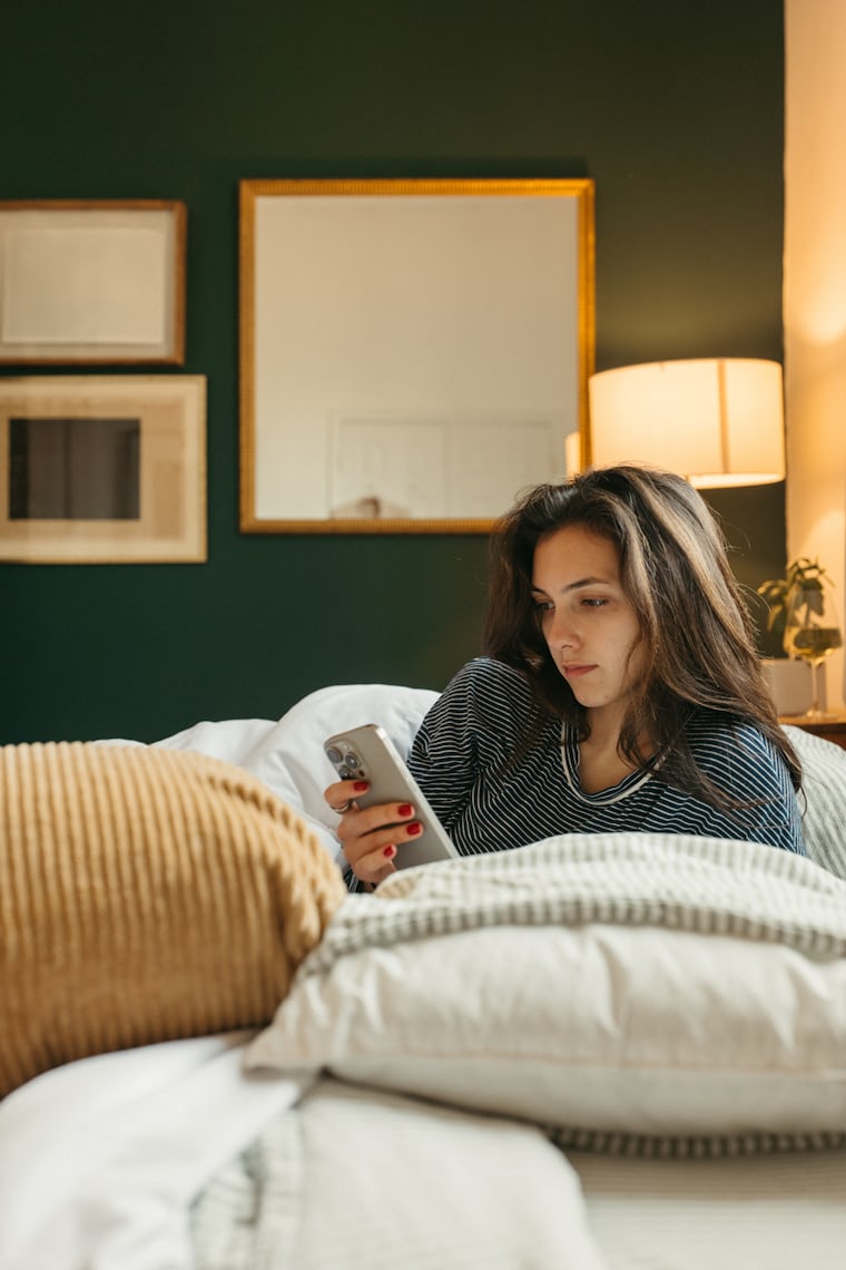Woman looking at phone in bed illustrating unhealthy screen habits before sleep