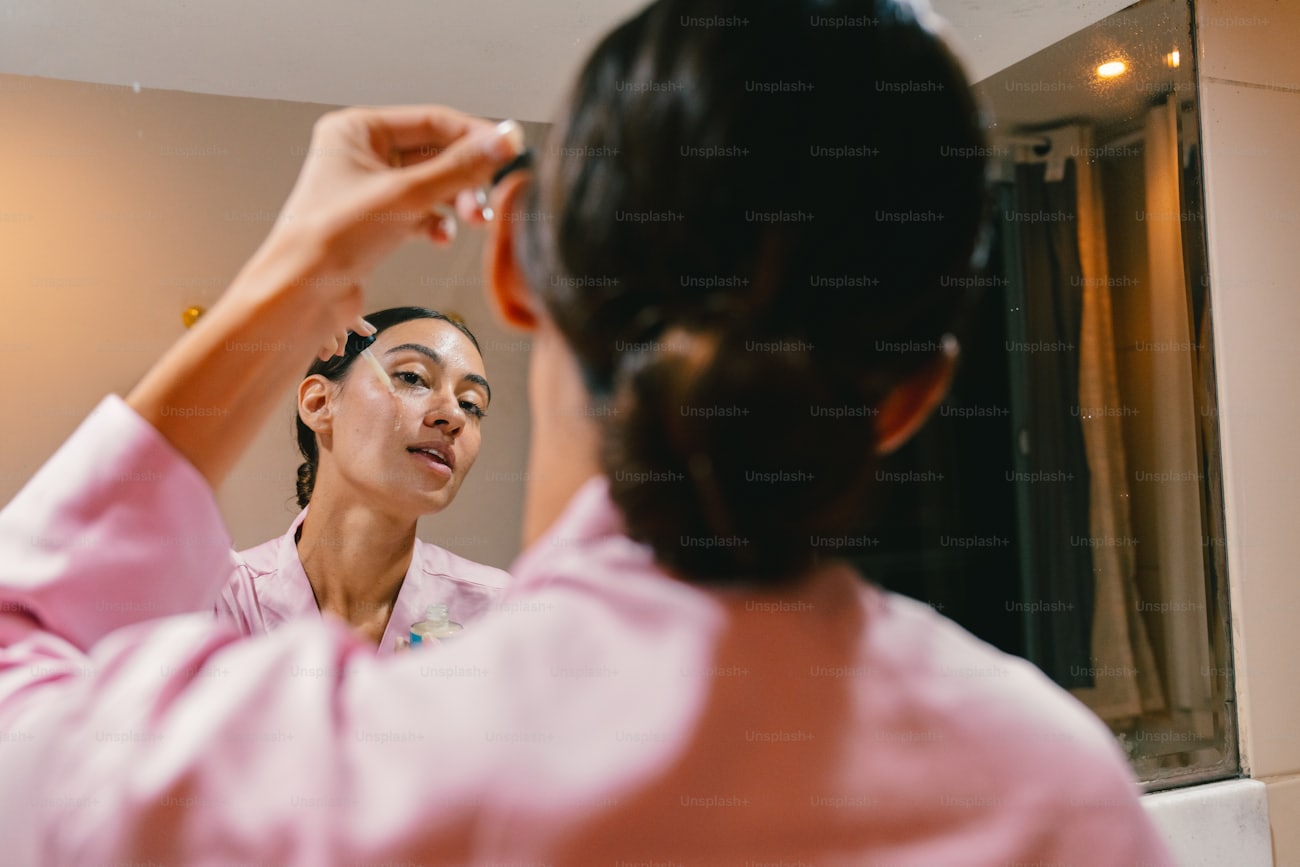 Woman applying facial serum in mirror as part of skincare routine