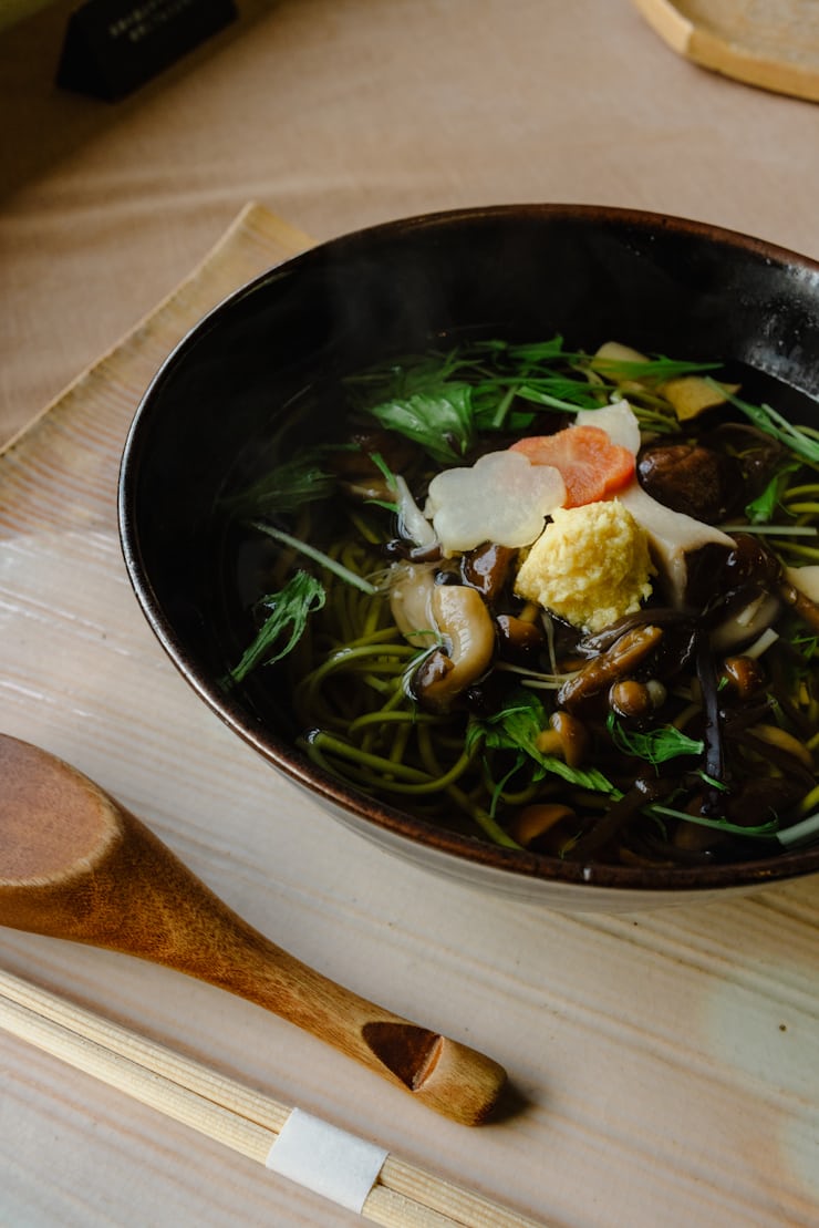 Steaming bowl of soba noodles with mushrooms and herbs for cozy healthy meal