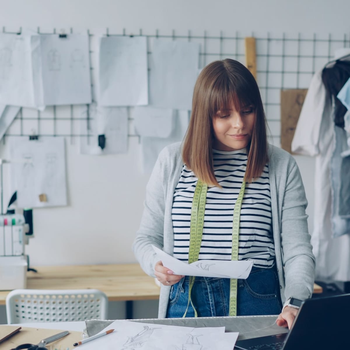Fashion designer working on laptop with sketches, representing AI-assisted design workflow